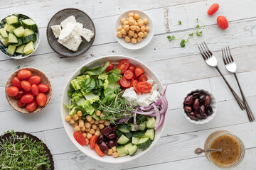 A large Greek salad bowl surrounded by smaller bowls of the ingredients.