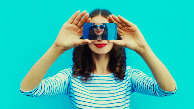 Close up of woman stretching her hands taking selfie picture by smartphone on blue background