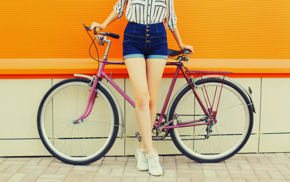 Summer image of legs of beautiful young woman in shorts posing with bicycle in the city on orange background