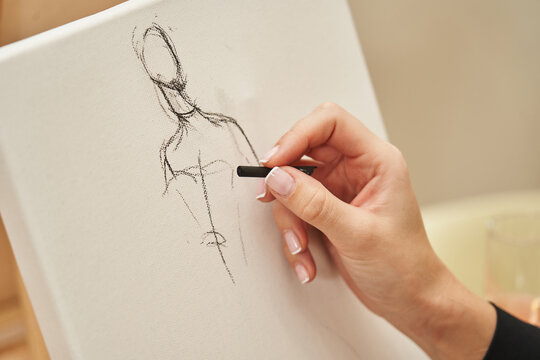 black chalk on white canvas female hand draws a sketch of a human figure