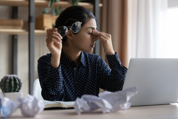 Tired millennial Indian business woman feeling headache, suffering from dry irritated eyes due to...