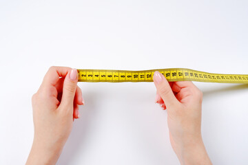 The woman's hands hold a yellow measuring tape on a white background.Measurement of length and...