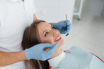 A young dentist examines and treats the teeth of a beautiful woman in modern white dentistry close-up. Dental prosthetics, treatment and teeth whitening. Modern dentistry.