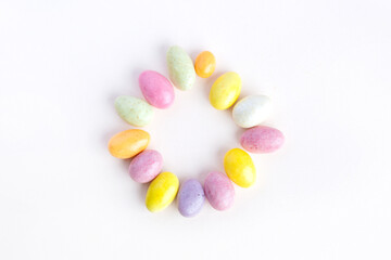 Easter circle made up of sweet colored chocolates. Delicate pastel pink background