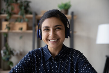 Head shot of happy Indian employee, businesswoman in headphones looking at camera, smiling, Video call close up portrait of female millennial blogger, coach, teacher giving training, consultation © fizkes