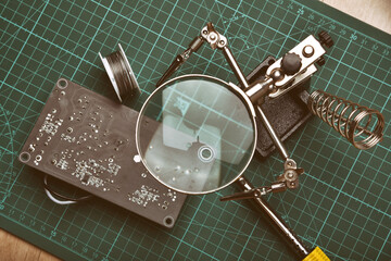 Electronics repair service, Technician fixing electronic circuit board with soldering iron and tin, Magnifying glass on soldering stand.