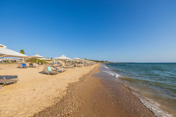 Beautiful view of Mediterranean coast line on bright summer day with empty sunbeds and umbrellas.  Greece. 