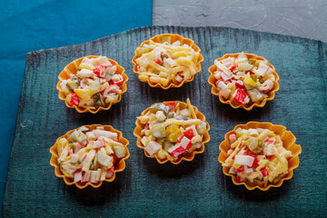 Salad with crab in tartlets on a beige plate on a black board.