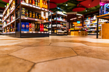Grocery store. Alcohol section. In the mall. Go shopping. Product selection. Daily worries. The era of consumption. Focus on the floor. Close-up view from the level of the floor tiles. - obrazy, fototapety, plakaty