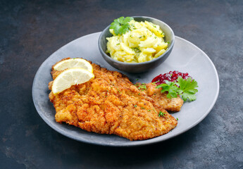 Traditionelles frittiertes Schnitzel mit Kartoffelsalat, Preiselbeeren und Zitronenscheiben...
