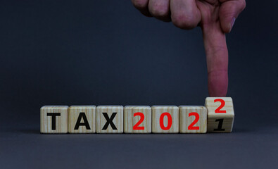 2022 tax new year symbol. Businessman turns a wooden cube and changes words Tax 2021 to Tax 2022. Beautiful grey table, grey background, copy space. Business, 2022 tax new year concept.