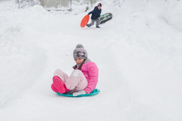 Children ride cheesecakes from a snow slide. Photo of an object in motion. Soft focus.