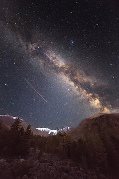 Starry sky and milky way over mountains. Flying meteor. Super wide angle. A large number of small stars throughout the image field. Soft focus on the stars.