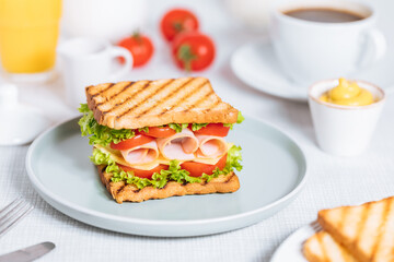 Toast sandwich with gouda cheese and turkey ham filled with tomato and lettuce on a bright background with ingredients in blurry background. Served with coffee and orange juice and eggs
