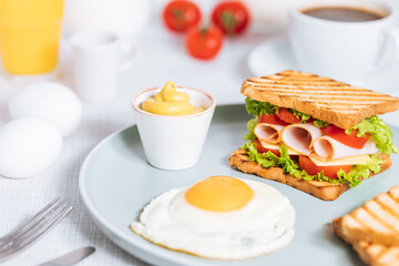 Toast sandwich with gouda cheese and turkey ham filled with tomato and lettuce on a bright background with ingredients in blurry background. Served with coffee and orange juice and eggs
