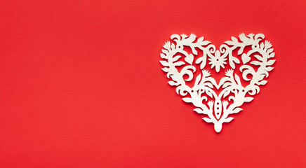 Festive composition with openwork white heart on red background. Top view, copy space. Valentine's day concept.
