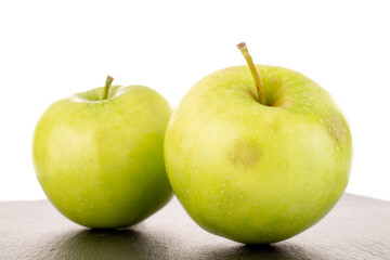 Two sweet green apples on a slate stone, close-up, isolated on white.