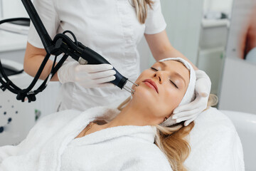 A young girl gets a charcoal peeling for the skin of the face in a beauty salon. Laser pulses...