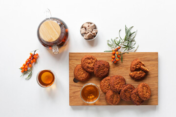 Herbal health tea with herbs and sea buckthorn in a glass teapot. On a white table, glass cups for tea and cereal cookies with dried apricots, raisins, nuts on a wooden board. Tea time. 