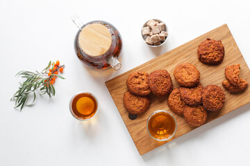 Vitamin tea with herbs and sea buckthorn, cereal gluten-free cookies with dried fruits on a wooden board. Healthy food, tea drinking.
White table, top view, copy space. 