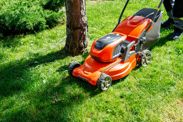 Obraz na płótnie Canvas orange lawn mower on wheels on green fresh grass. grass mowing process