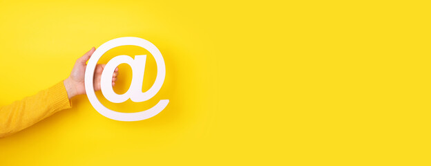 hand holding email symbol over yellow background, panoramic layout