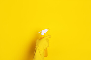hand in a glove with a spray bottle over yellow background, cleaning concept