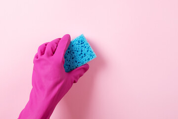 A hand in a pink rubber glove holds a blue  washing sponge over pink background
