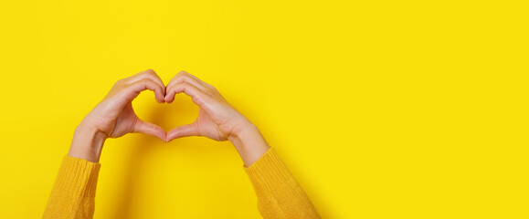 Hands making heart shape, love symbol over yellow background, panoramic layout