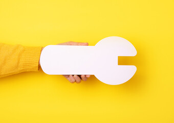 white wrench in hand, repair symbol in hand over yellow background