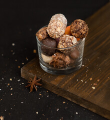 A mixture of chocolate truffles in a glass bowl on a dark background. Desserts made from a mixture of sweet candies. Improper diet from harmful foods. The risk of tooth decay and obesity.