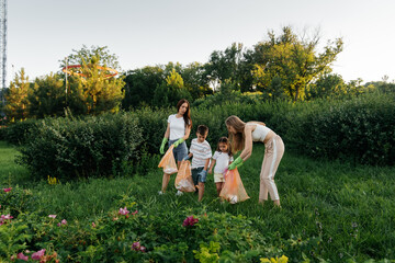 A group of adults and children together at sunset is engaged in garbage collection in the park....
