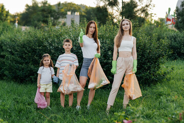 Fototapeta premium A group of adults and children together at sunset is engaged in garbage collection in the park. Environmental care, waste recycling. Sorting garbage.