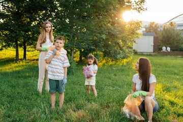 A group of adults and children together at sunset is engaged in garbage collection in the park....