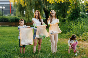 Fototapeta premium A group of adults and children together at sunset is engaged in garbage collection in the park. Environmental care, waste recycling. Sorting garbage.