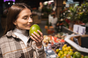 Portrait of a young woman who sniffing fresh mango in a supermarket. Girl buys fruit at the grocery...