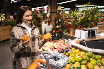 Young happy woman choosing exotic kiwano fruit in supermarket. Girl in the fruit department of a grocery store