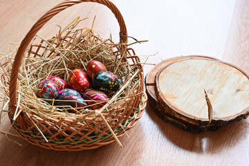 Old wooden Easter eggs in a wicker basket on hay.