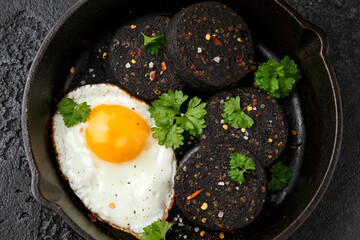 Cooked Black Pudding with egg, herbs and parsley on iron cast pan