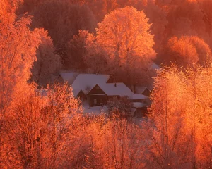 Fotobehang Rood Winterdorp in een bergbos in de sneeuw bij zonsondergang