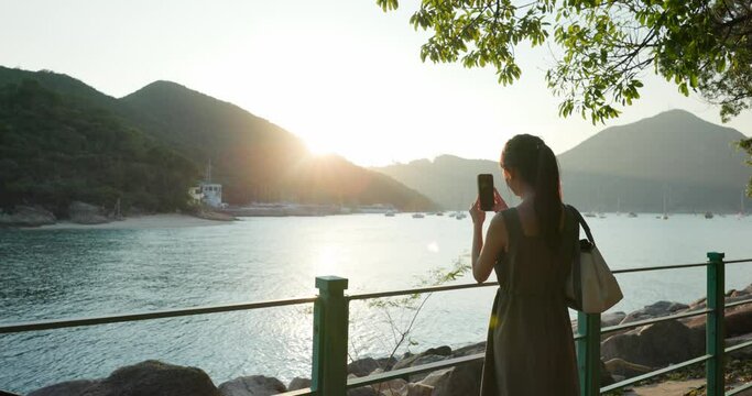 Woman use cellphone to take photo with sunset sea view