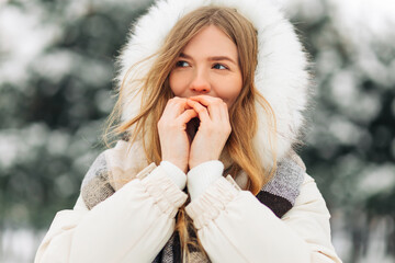 girl warming up her hands in warm winter clothes. Attractive model portrait outdoors on a cold day