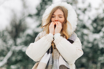 girl warming up her hands in warm winter clothes. Attractive model portrait outdoors on a cold day