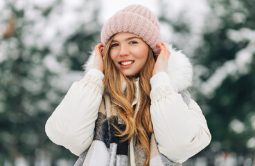 happy woman, in a warm knitted scarf and hat looking at the camera, woman posing in the street in a snowy winter park