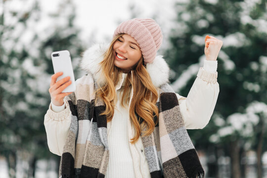 Woman On The Street In Winter, Screaming And Clenching Her Fist, Holding A Mobile Phone In Her Hands Victory