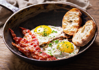 Breakfast with pan of fried eggs, bacon, toasts