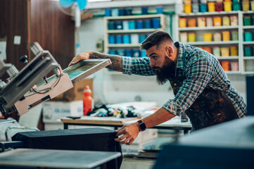 Male worker using printing machine in a workshop