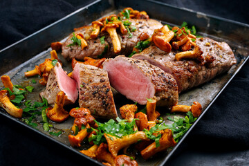 Gebratenes dry aged Schweinefilet Chateaubriand Medaillon Steak natur mit Pfifferlingen und Petersilie serviert als Draufsicht auf einem rustikalen Metall Tablett auf schwarzem Hintergrund
