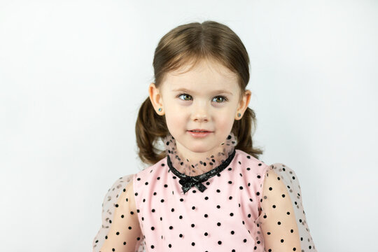 Smiling little girl with two ponytails in a dress with polka dots on a white background reproachfully looks to the side. Studio photo