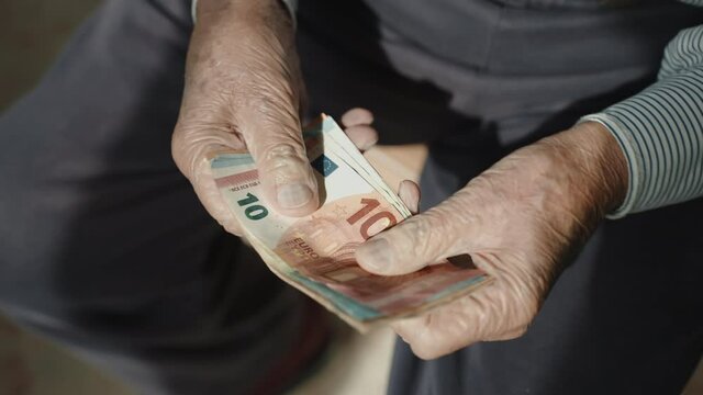 Old italian pensioner holding stack of euro banknotes in his wrinkled hands, senior man counting money savings and pension income. Low budget of grandfather, financial planning of old man in
